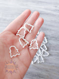 Hand holding white ghost 3D printed stitch markers on a wooden surface