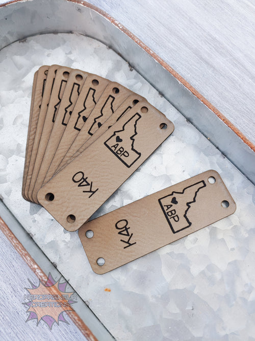 Set of faux leather tags with engraved designs and text on a textured surface