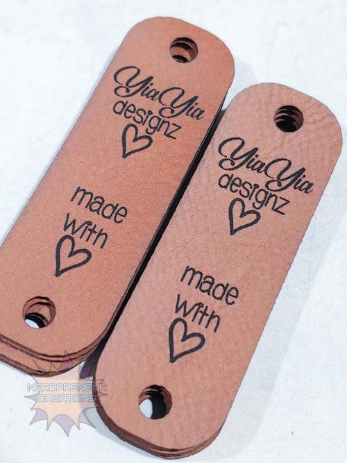 Two brown leather tags with 'Yia Yia designz' and 'made with love' text on a white background.