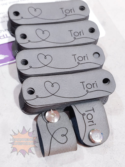 Set of gray tags with 'Tori' printed on them, some with decorative hearts and gemstones.