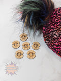 Wooden bear-shaped buttons on a white surface with a colorful knitted item and feather in the background.