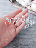Hand holding small white 3D printed stitch markers on a wooden surface with cotton in the background.