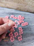 Hand holding a pink cross 3D printed stitch markers on a wooden surface