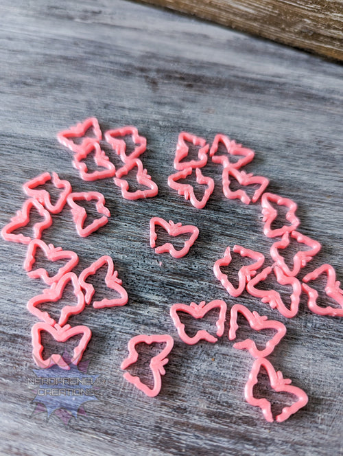Pink butterfly 3D printed stitch markers on a wooden surface