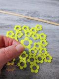 Hand holding yellow flower 3D printed stitch marker on a gray surface