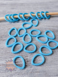 Blue 3D printed stitch markers on a wooden stick against a gray wooden background