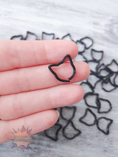 Black cat 3D printed stitch markers held between fingers with more clips in the background.