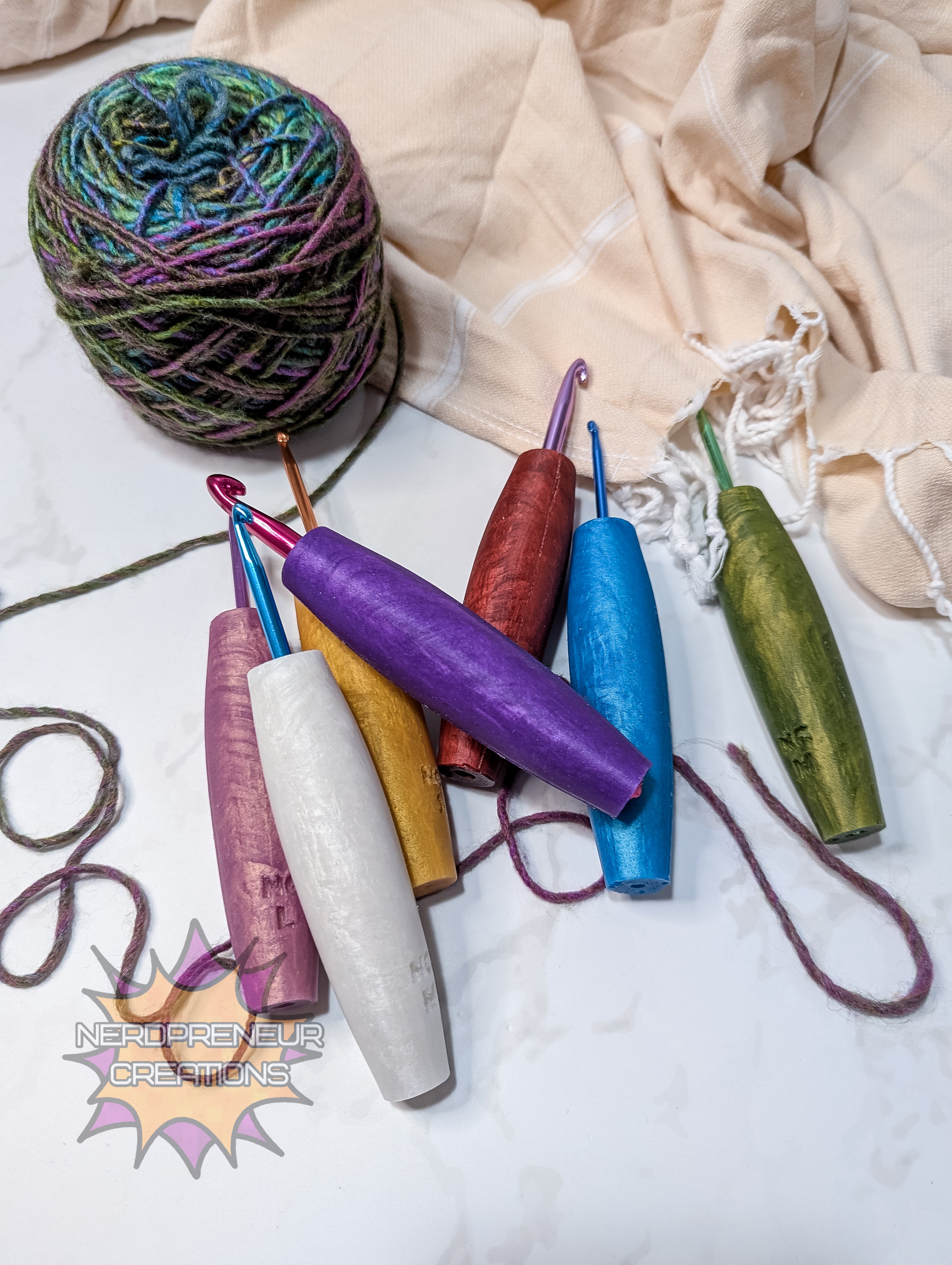 Colorful yarn and silicone crochet grips on a textured surface with 'Nerdpreneur Creations' branding