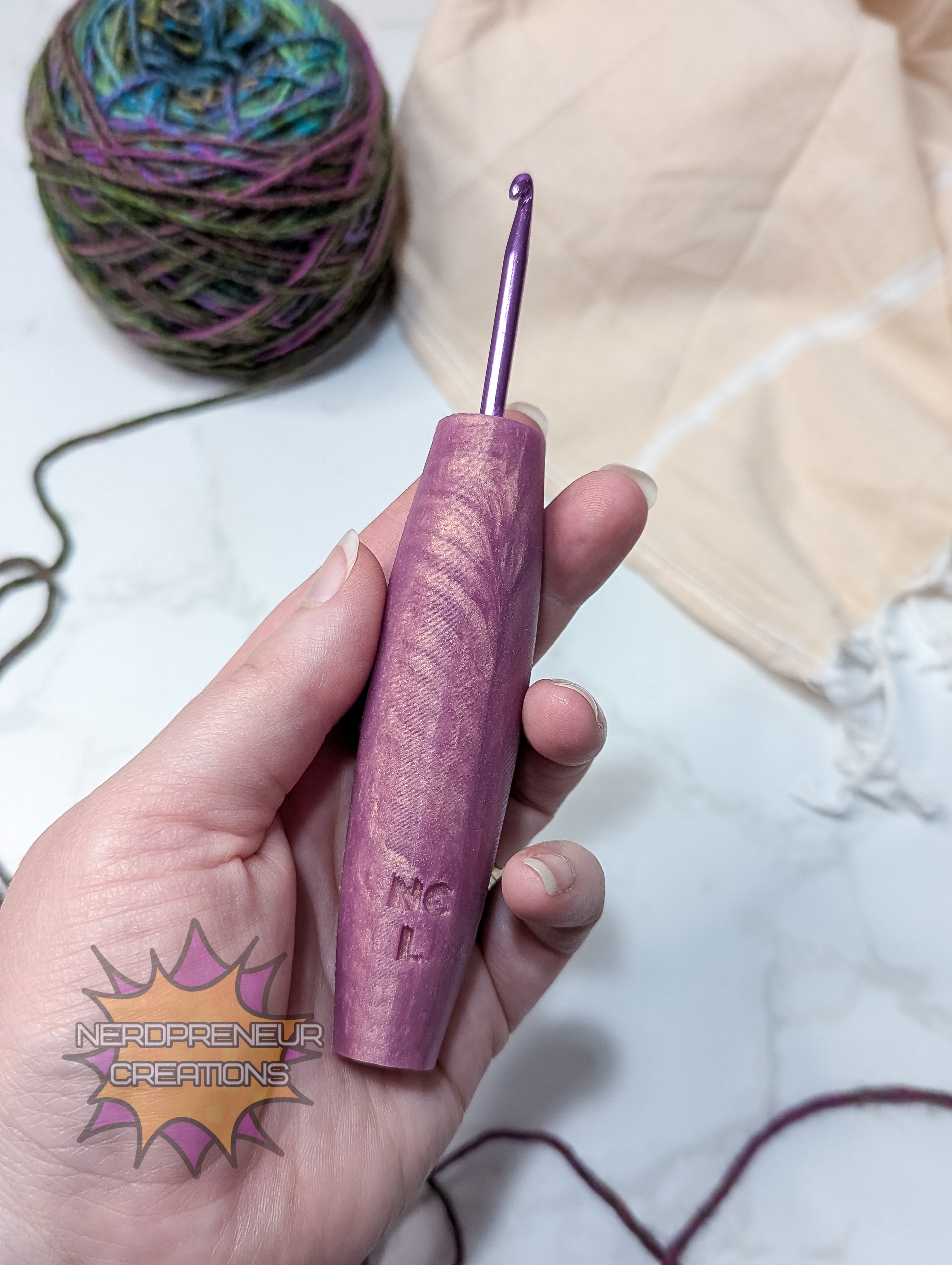 Purple crochet hook held in a hand with yarn and fabric in the background