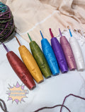 Set of colorful silicone crochet hooks on a textured fabric background with a brand logo.