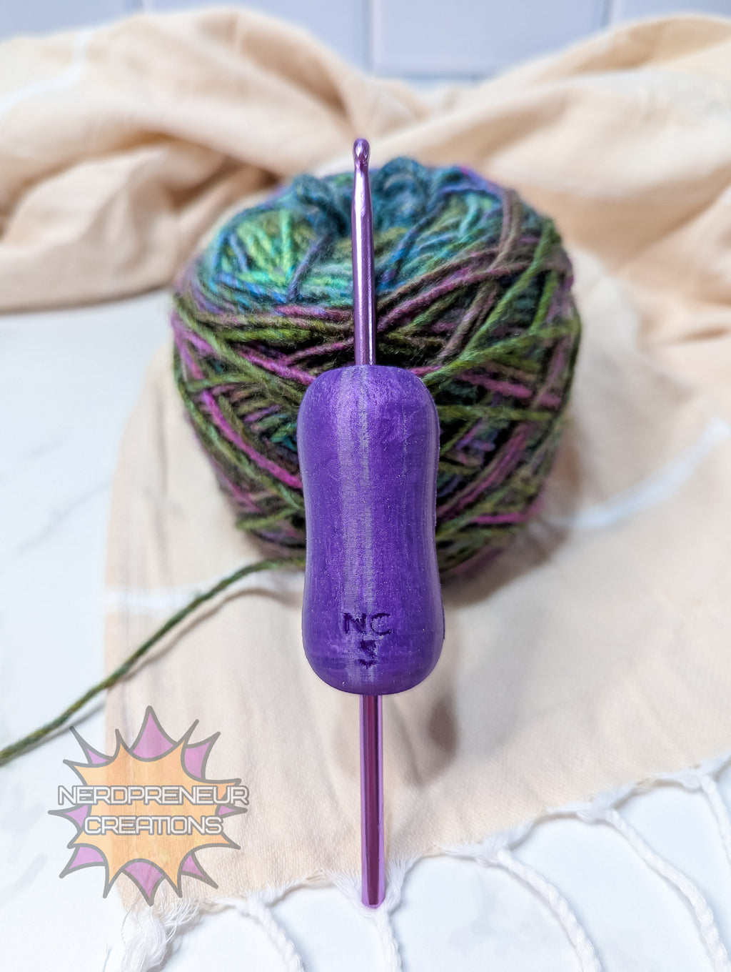 Purple silicone crochet grip with a ball of multicolored yarn on a beige blanket.