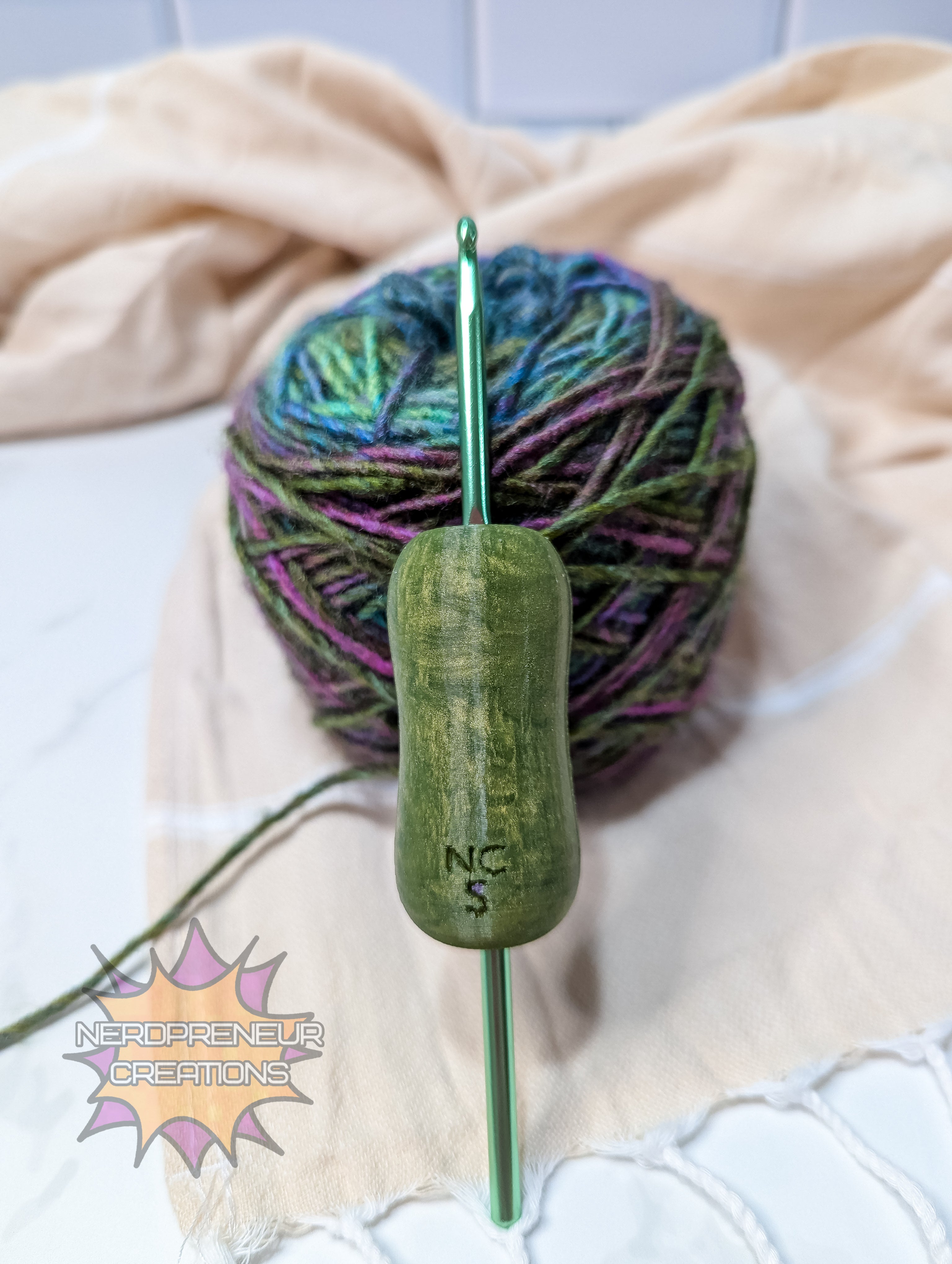 Green silicone crochet grip with a ball of yarn on a beige blanket, featuring 'Nerdpreneur Creations' logo.