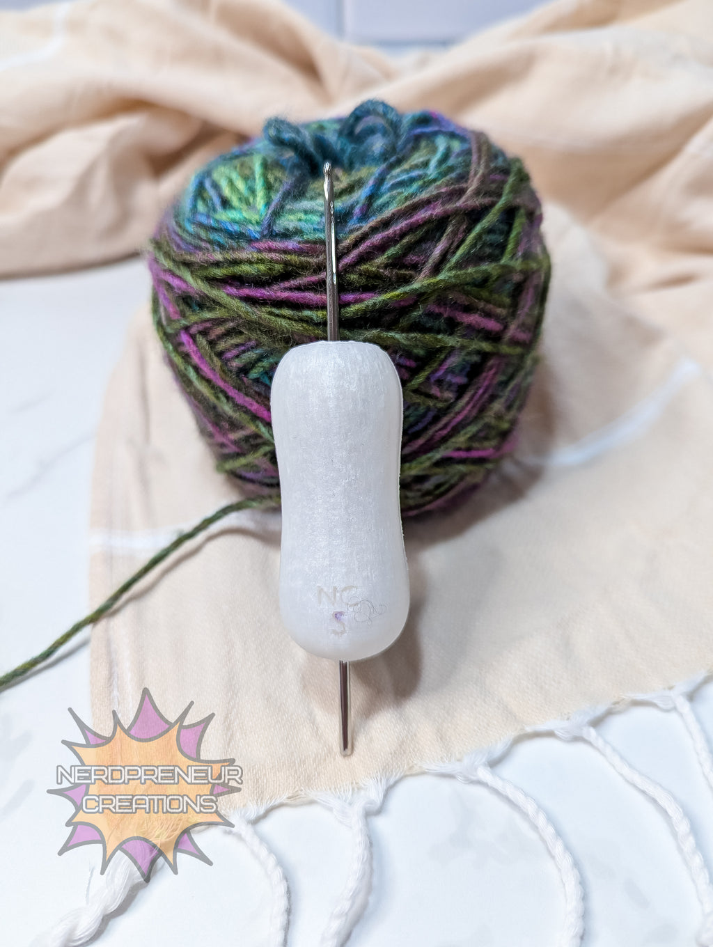 Ball of yarn with a silicone crochet grip on a textured surface, featuring 'Nerdpreneur Creations' logo.