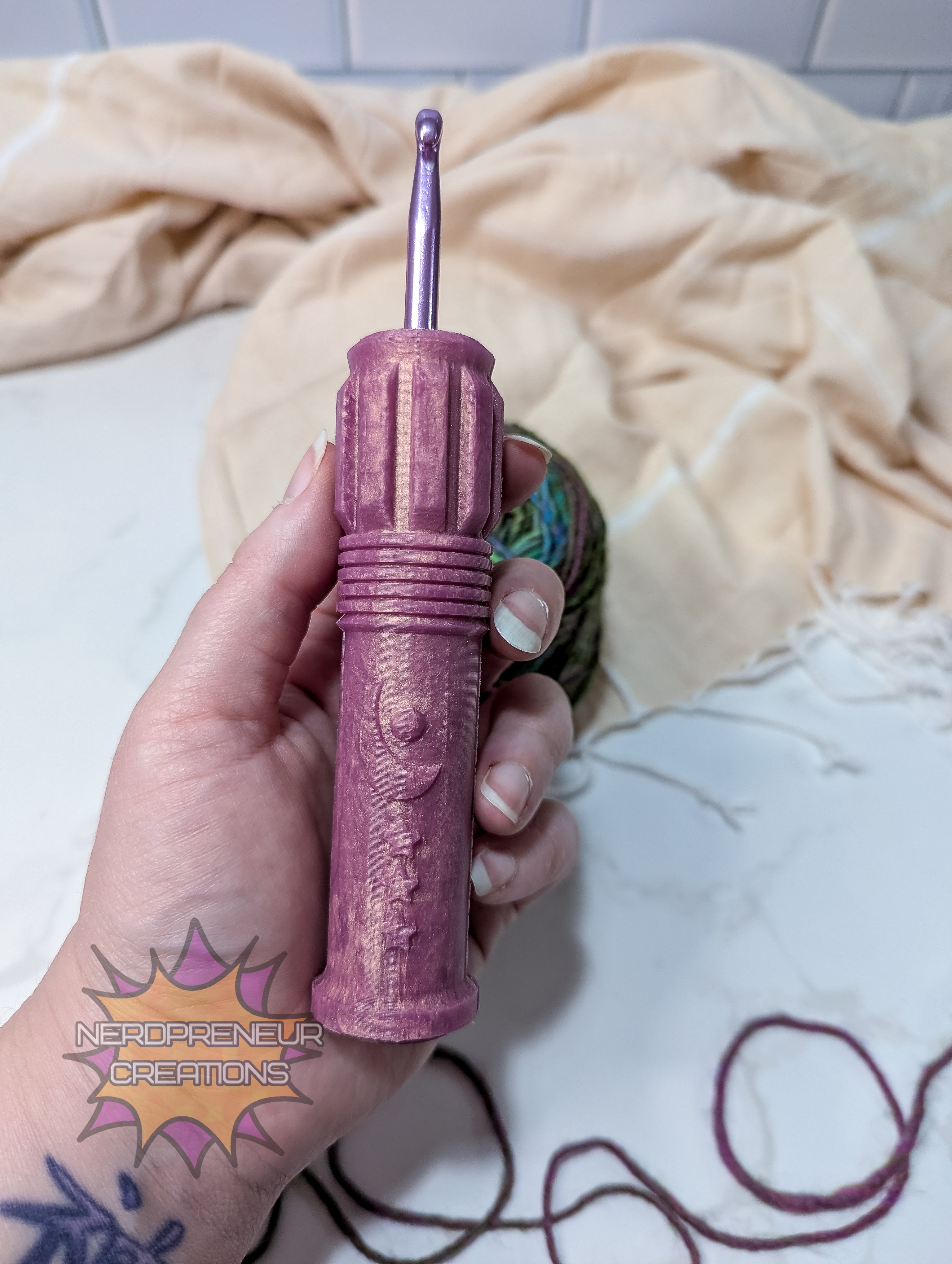 Pink silicone crochet grip held by a hand with tattoos on a light-colored blanket.