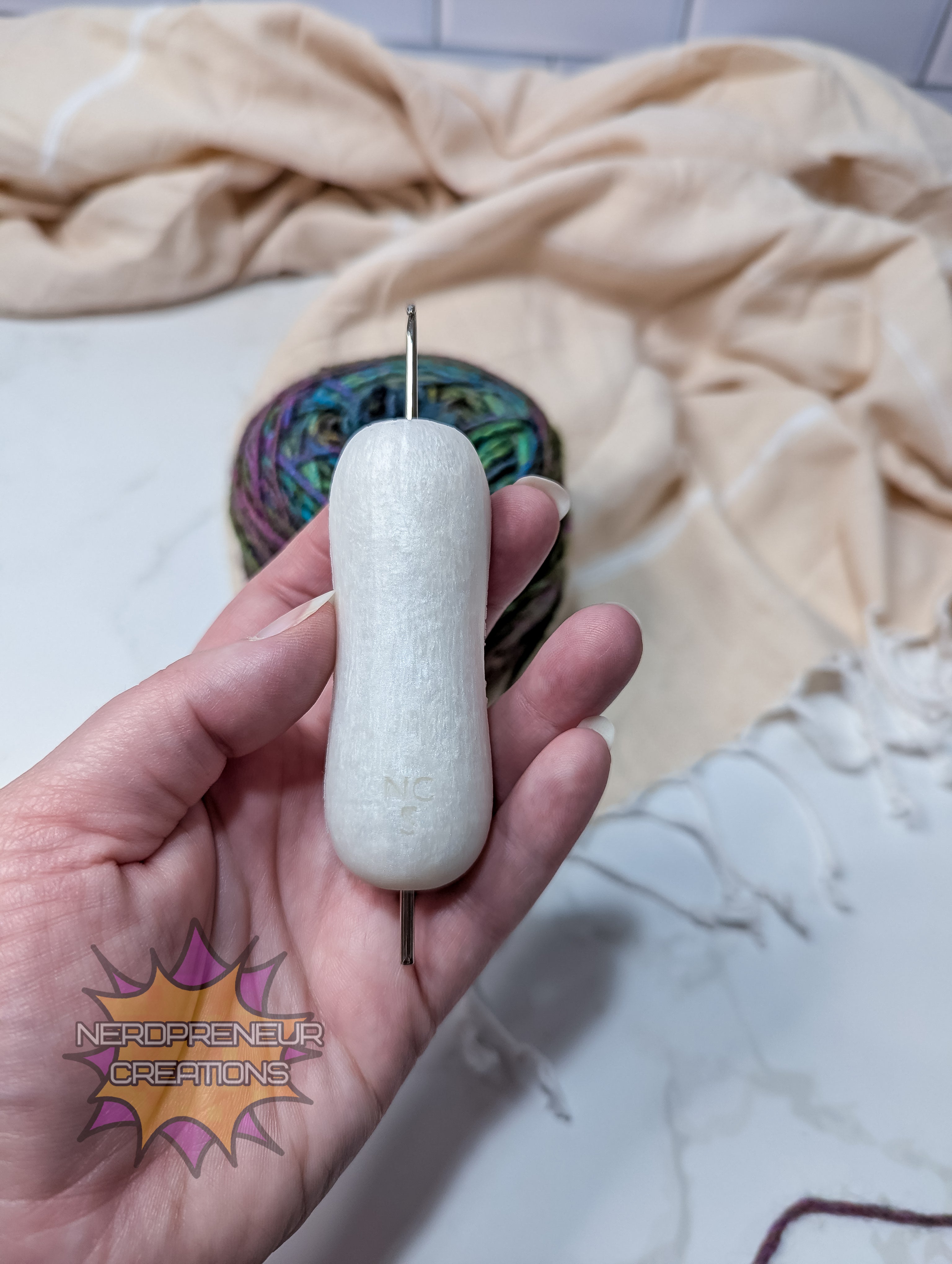 Hand holding a white silicone crochet grip, against a patterned fabric background.