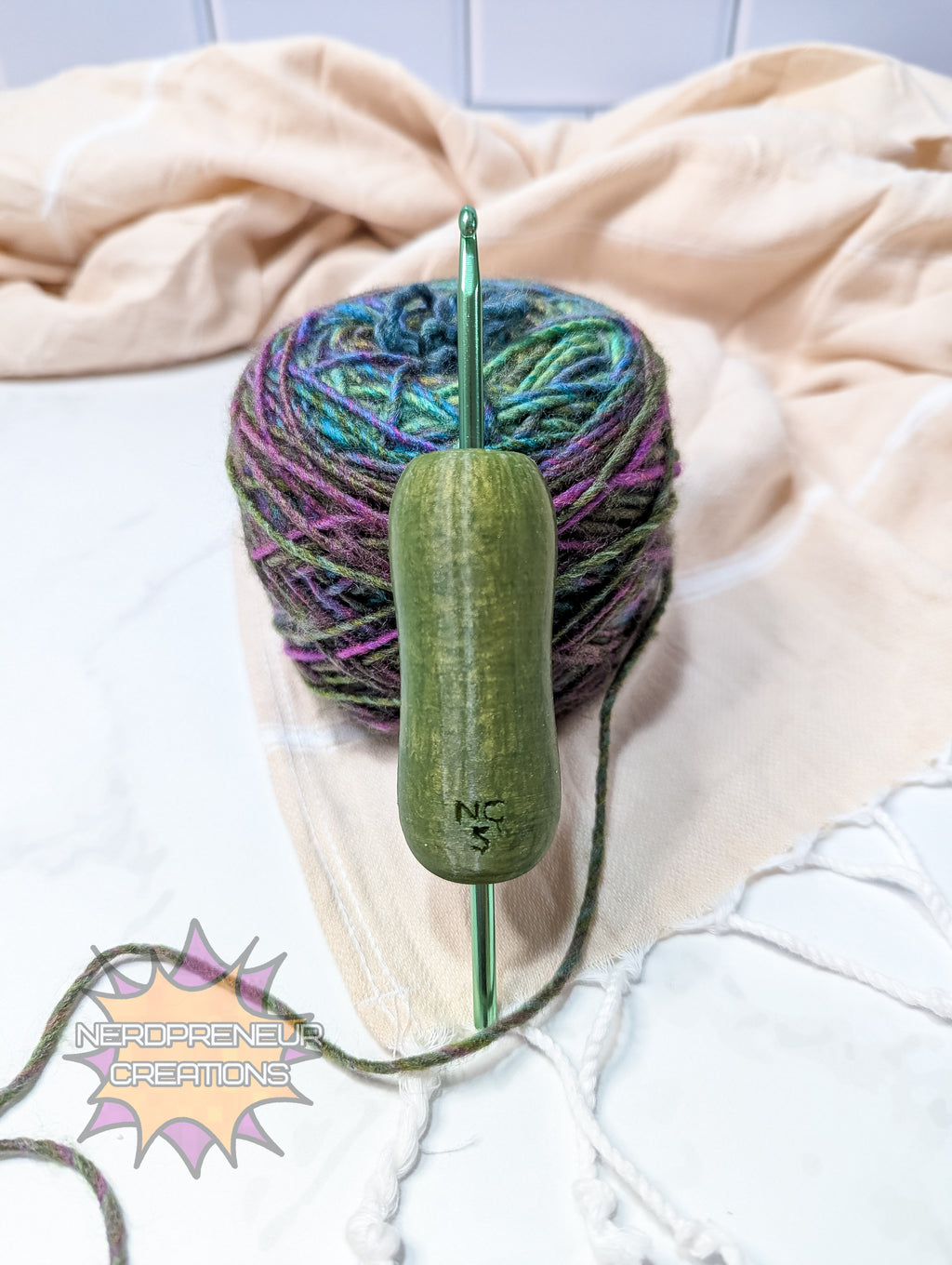 Ball of yarn with a green silicone crochet grip on a light pink blanket