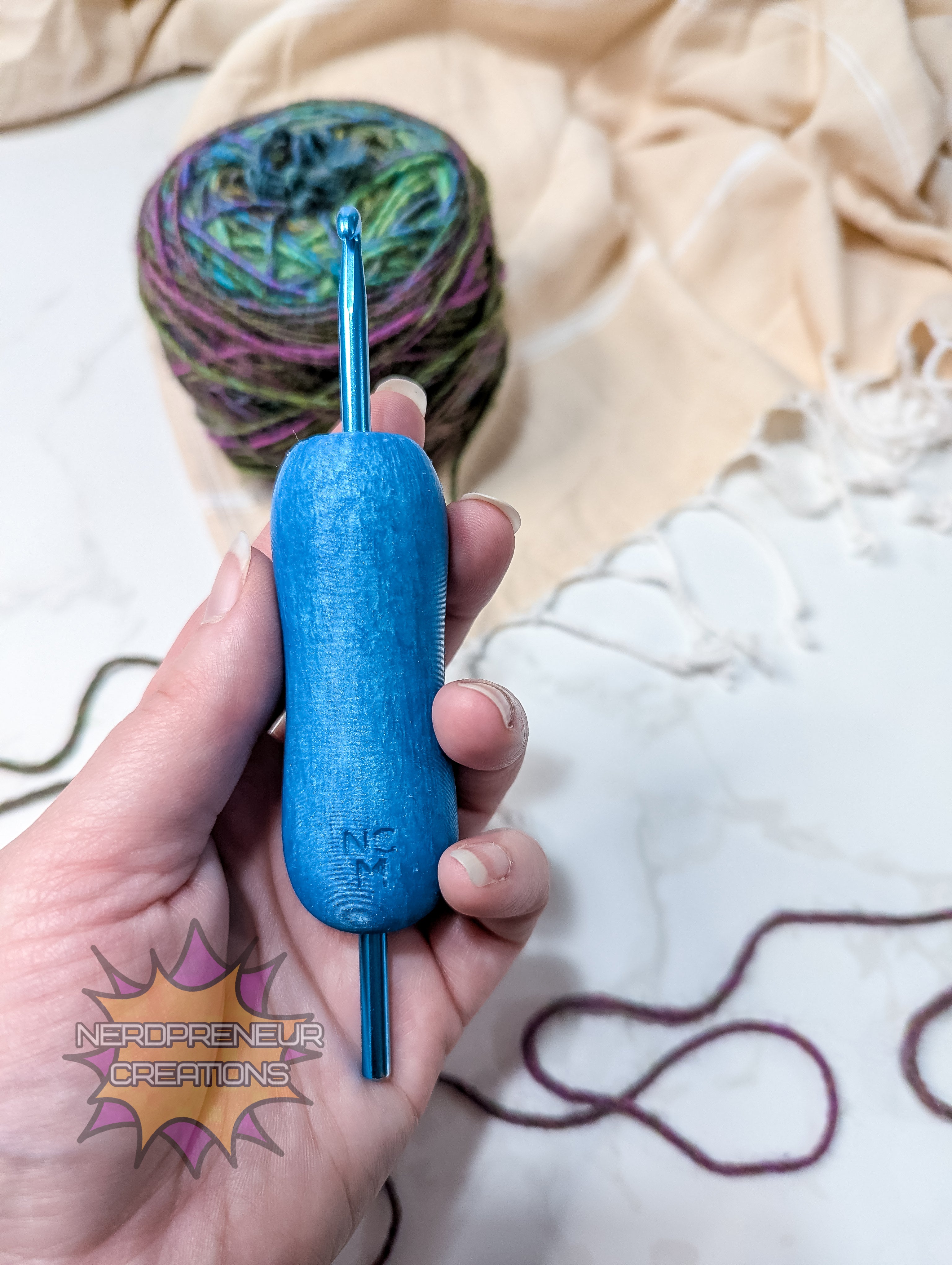 Blue silicone crochet grip held in a hand with yarn and fabric in the background
