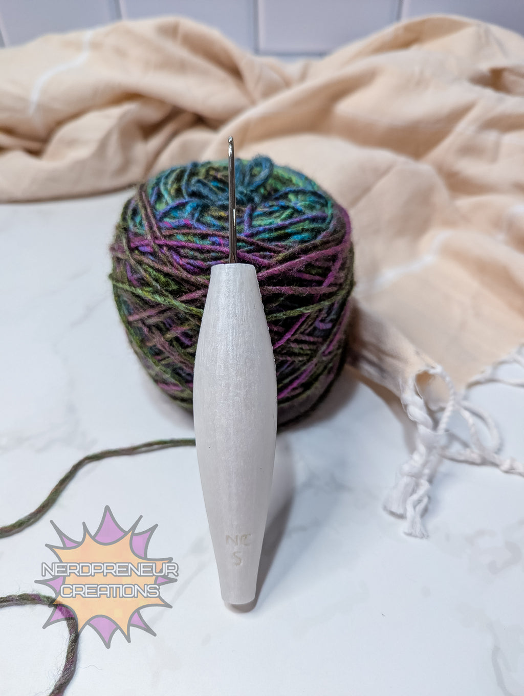 Ball of yarn with a silicone crochet grip on a textured surface, featuring the brand 'Nerdpreneur Creations'.