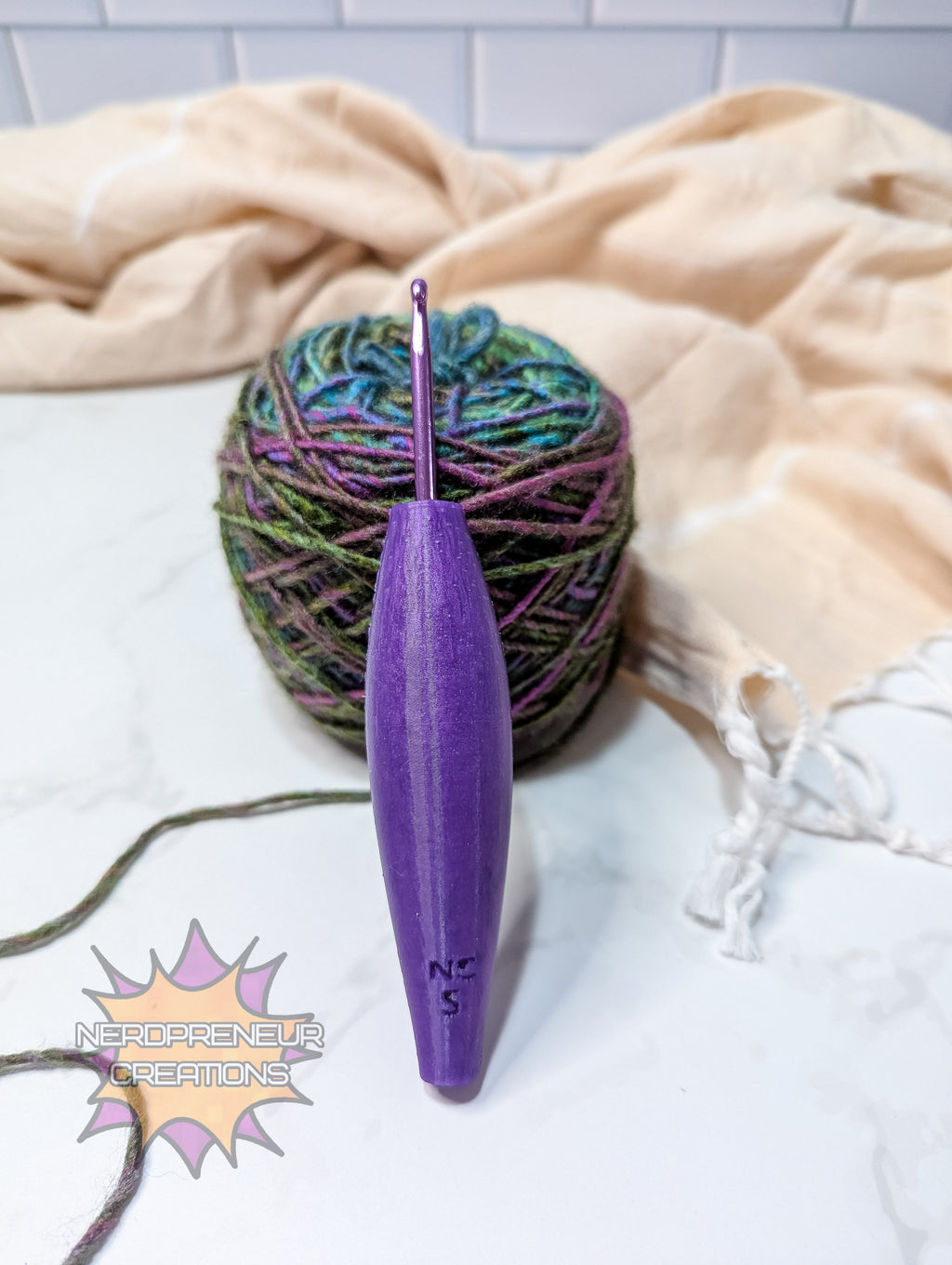 Purple silicone crochet grip next to a ball of multicolored yarn on a white surface with a beige towel in the background.