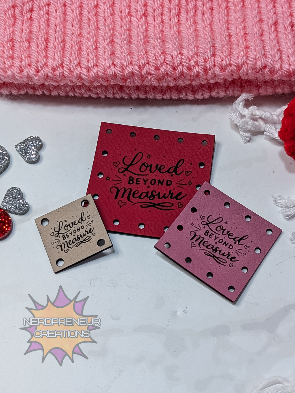 Red faux leather patches with 'Loved Beyond Measure' text on a white surface with pink fabric in the background.