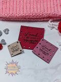 Red faux leather patches with 'Loved Beyond Measure' text on a white surface with pink fabric in the background.