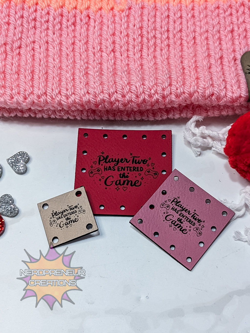 Decorative faux leather patches with "You're my favorite Player 2" text on a white surface with pink fabric and red flower.