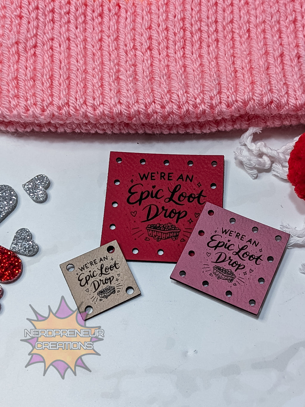 Three square faux leather patches with 'Epic Loot Drop' text on a textured surface with pink fabric and decorative items.