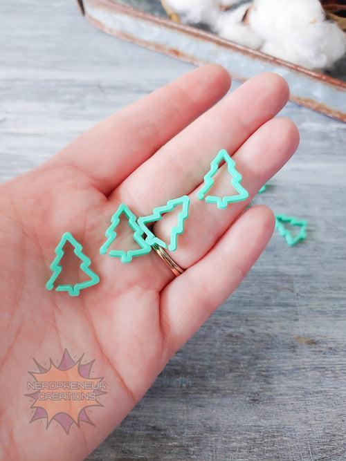 Green Christmas tree 3D printed stitch markers on a hand with a wooden surface in the background
