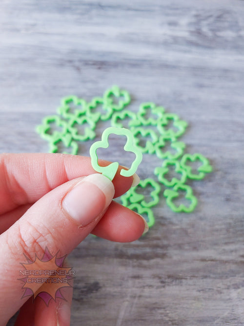 Hand holding a green clover 3D printed stitch marker on a wooden surface